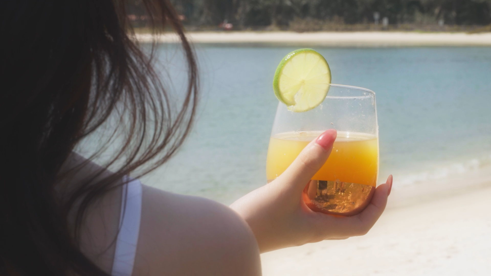 An over-the-shoulder shot of a lady holding a glass of mango mocktail.
